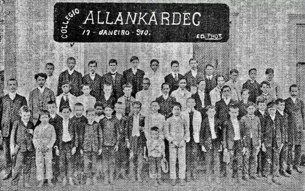 Fotografia antiga de alunos e professores diante do Colégio Allan Kardec, com a placa de 17 de janeiro de 1910