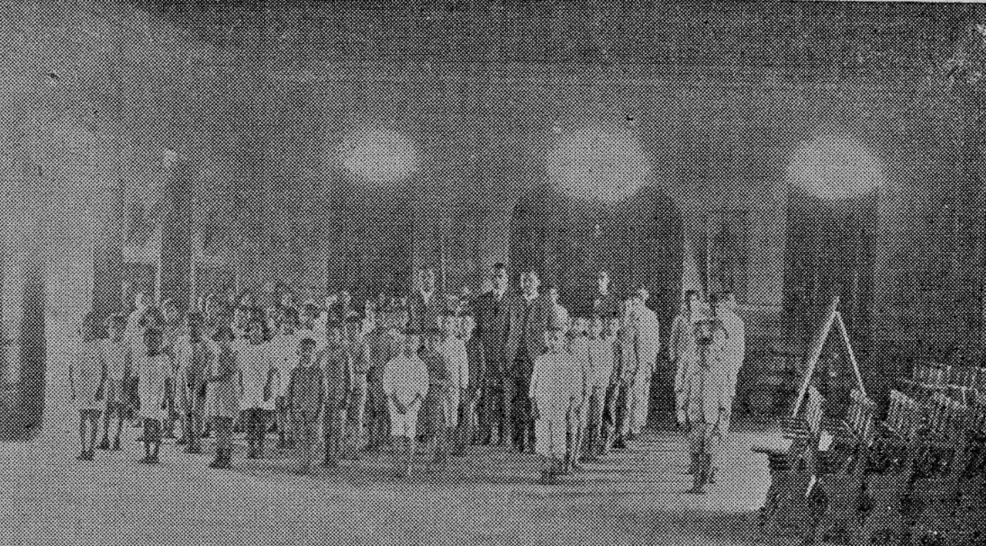 Fotografia antiga e desfocada de alunos em fila sob o corredor do Colégio Allan Kardec
